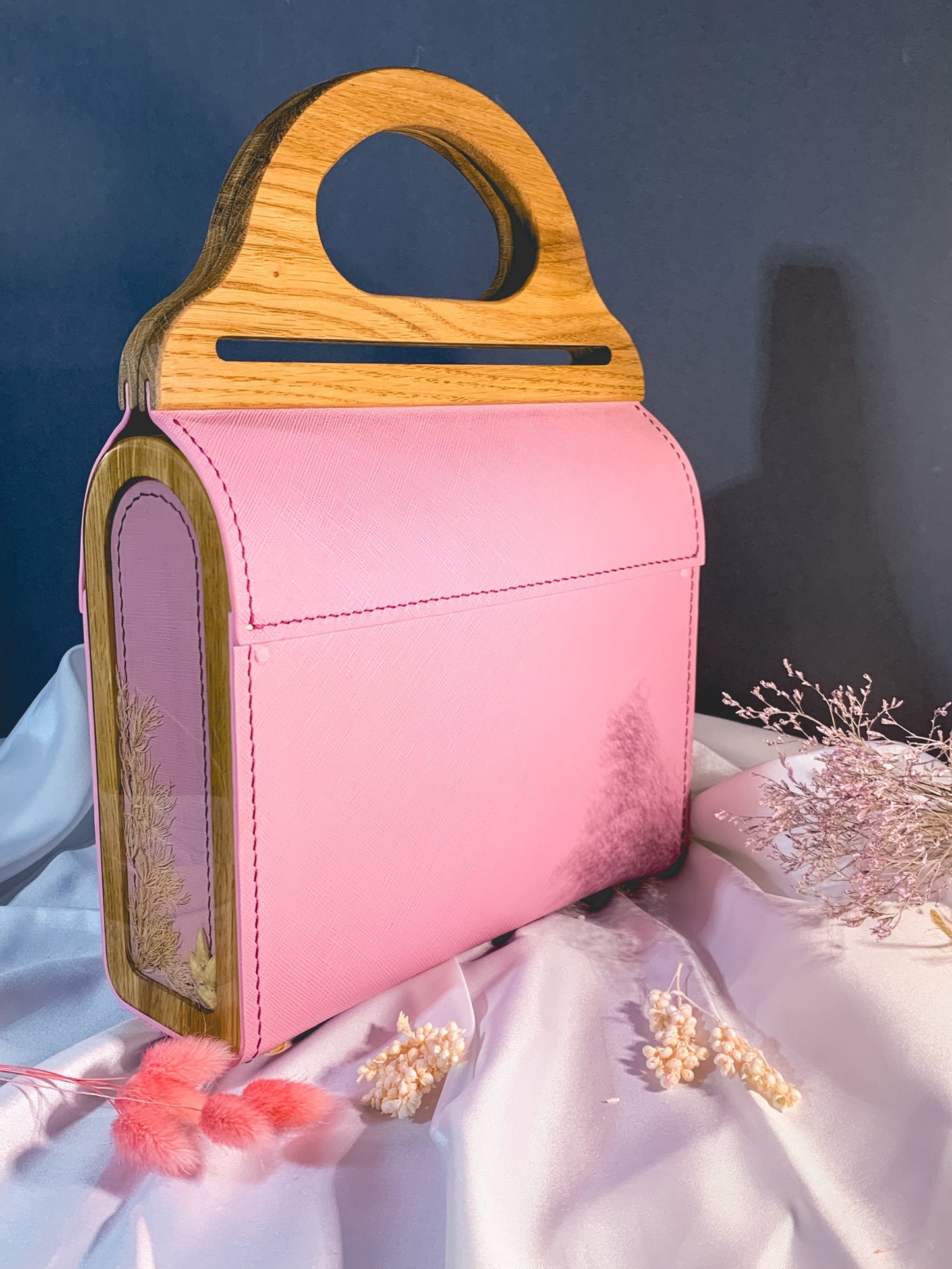 A handmade bag with natural leather, an oak handle, and epoxy resin inserts with dried flowers.